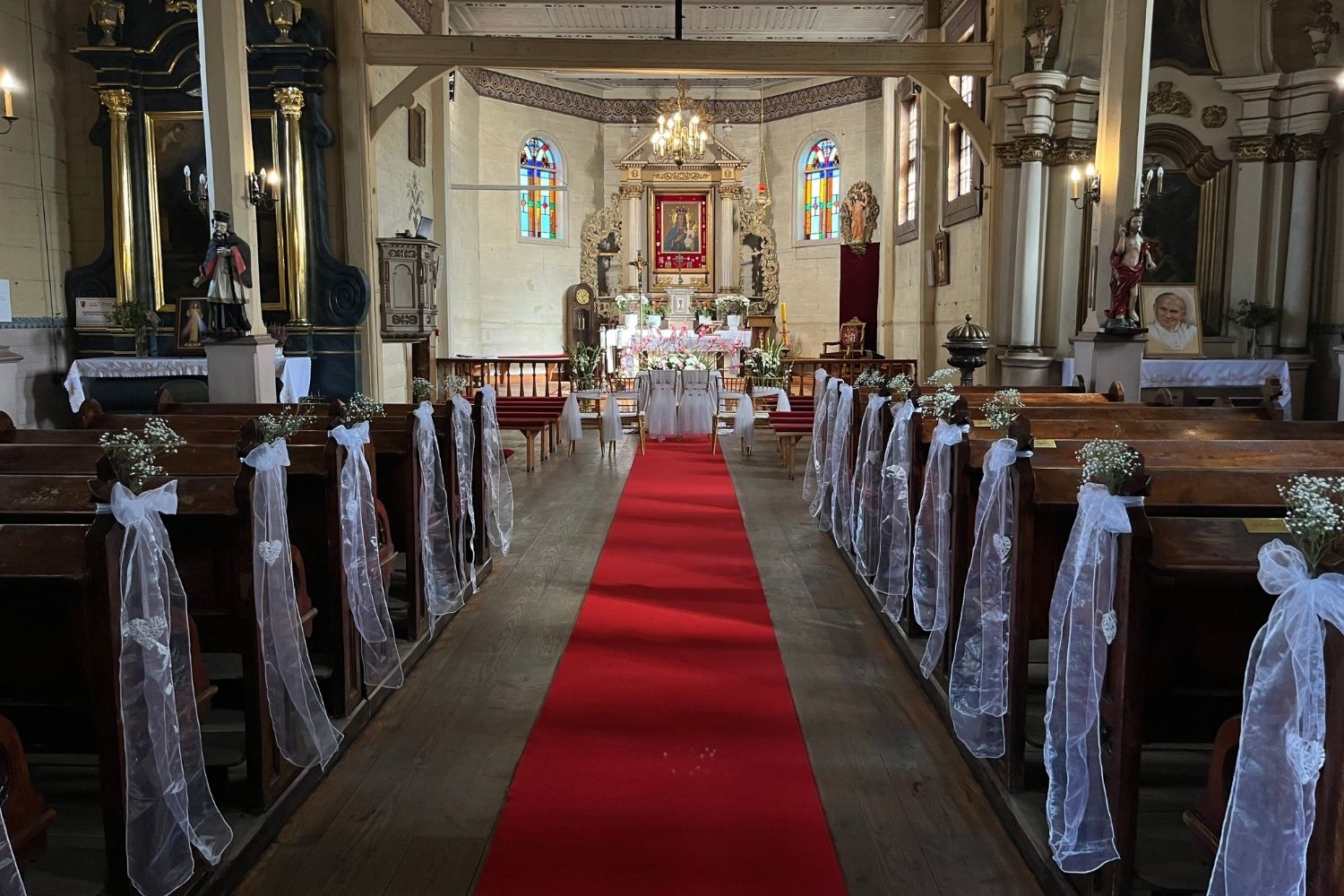 Nawa główna kościoła udekorowana na ślub, czerwony dywan, tiul i lampiony