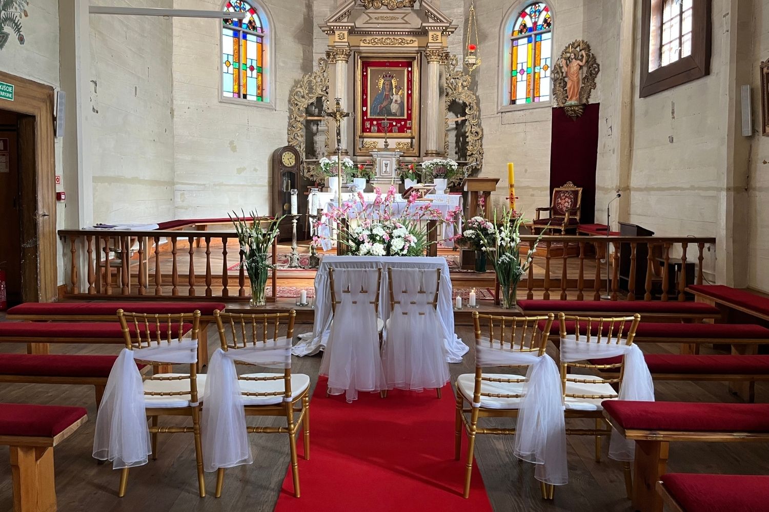 Dekoracja ołtarza w kościele na ślub, złote krzesła i kwiaty, czerwony dywan