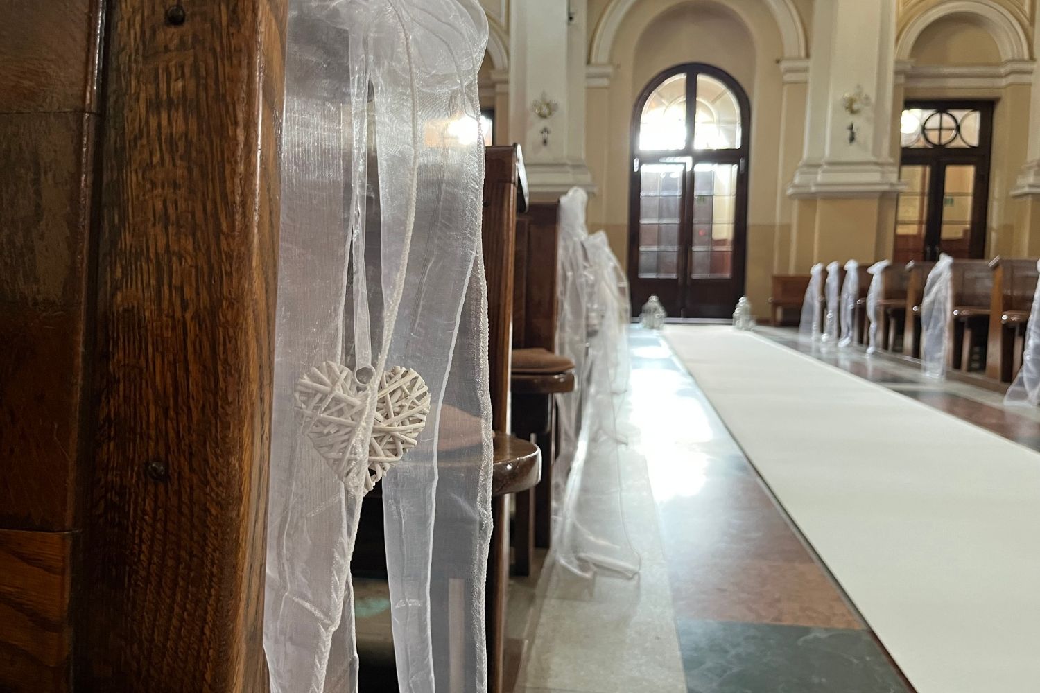 Dekoracja ławki kościelnej na ślub, biały tiul i wiszące serce z wikliny