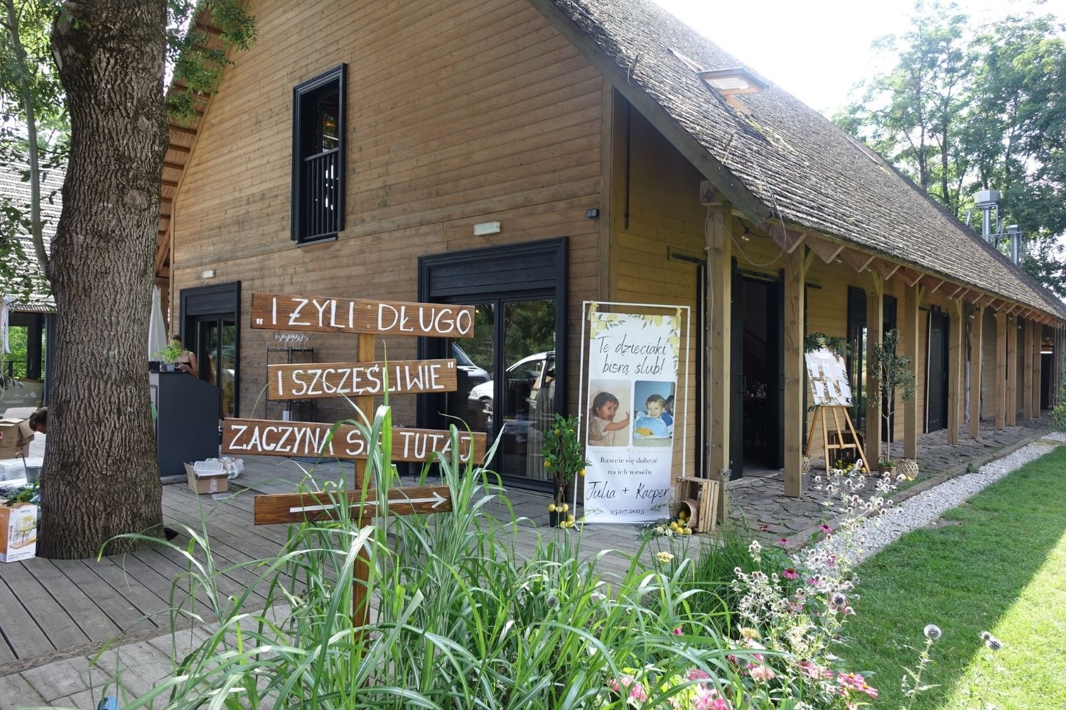 Dekoracje ślubne, Drewniane drogowskazy z napisami przed budynkiem weselnym, plener