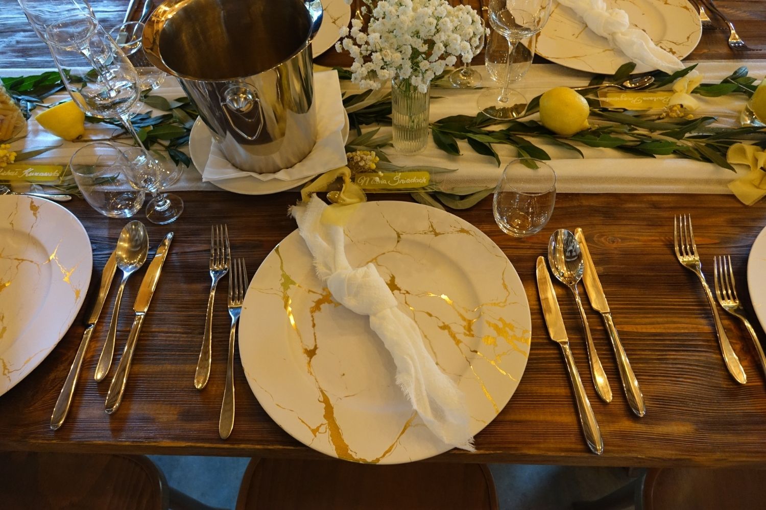 Zbliżenie na nakrycie weselne na drewnianym stole, biały talerz ze złotymi zdobieniami i dekoracja z cytryn.